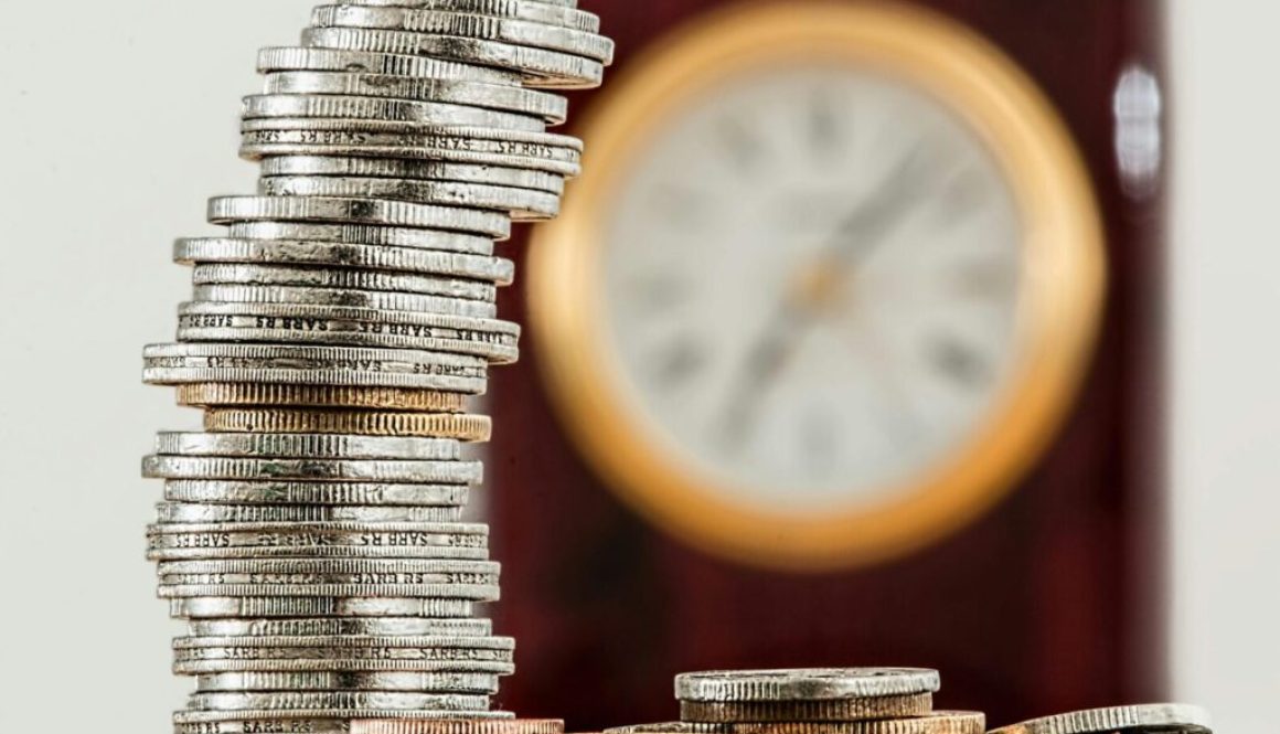 A close-up image of stacked coins with a blurred clock, symbolizing time and money relationship.