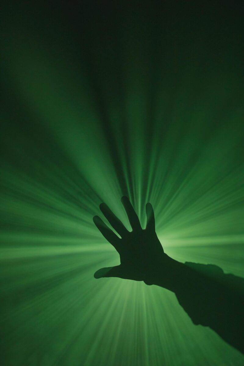 A mysterious silhouette of a hand reaching toward vibrant green light rays creating a dynamic visual effect.